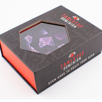 Void Weaver solid metal RPG dice set with purple and blue enamel displayed in a closed Tabletop Dominion box, showing intricate engraved polyhedral dice through the window.