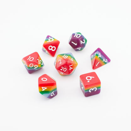 Rainbow Pride soft‑edge acrylic dice set arranged loosely on a white background, displaying all seven vibrant rainbow polyhedral dice.