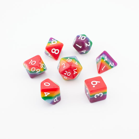 Rainbow Pride soft‑edge acrylic dice set arranged loosely on a white background, displaying all seven vibrant rainbow polyhedral dice.