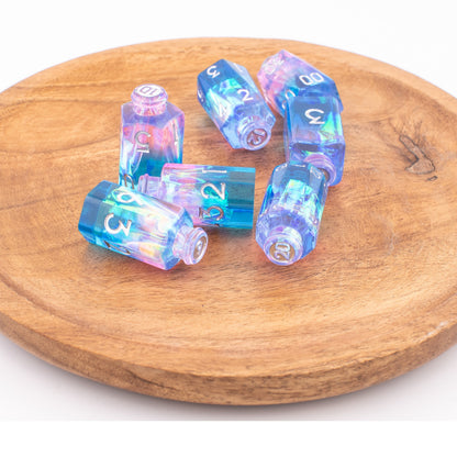 Tabletop Dominion Prismatic Elixir potion bottle dice displayed loose on a wooden tray with iridescent blue‑pink‑purple resin and white numbering.