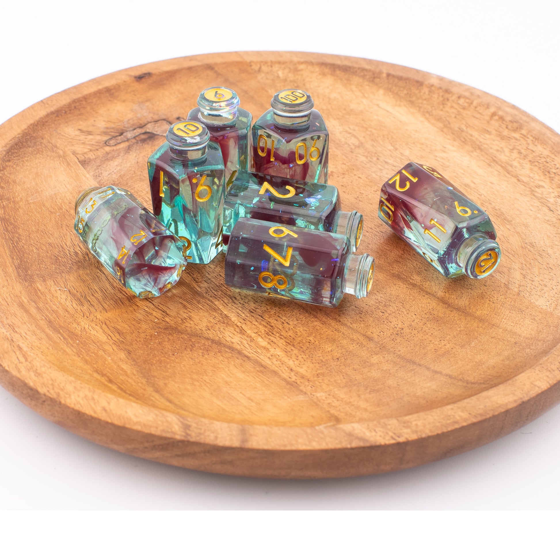 Tabletop Dominion Blood Alchemist potion bottle dice shown loose on a wooden tray, featuring colourful bottle‑shaped d12s with gold numbering.