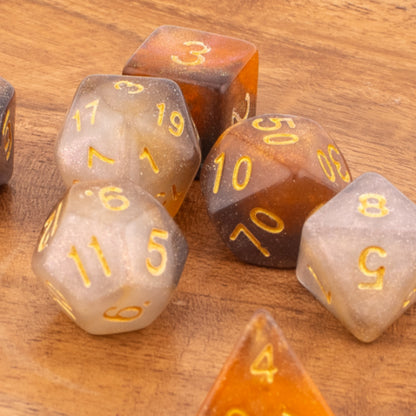 Clear Autumn acrylic dice scattered on a wooden surface, contrasting the warm wood grain with the translucent orange‑grey dice and gold numbering.