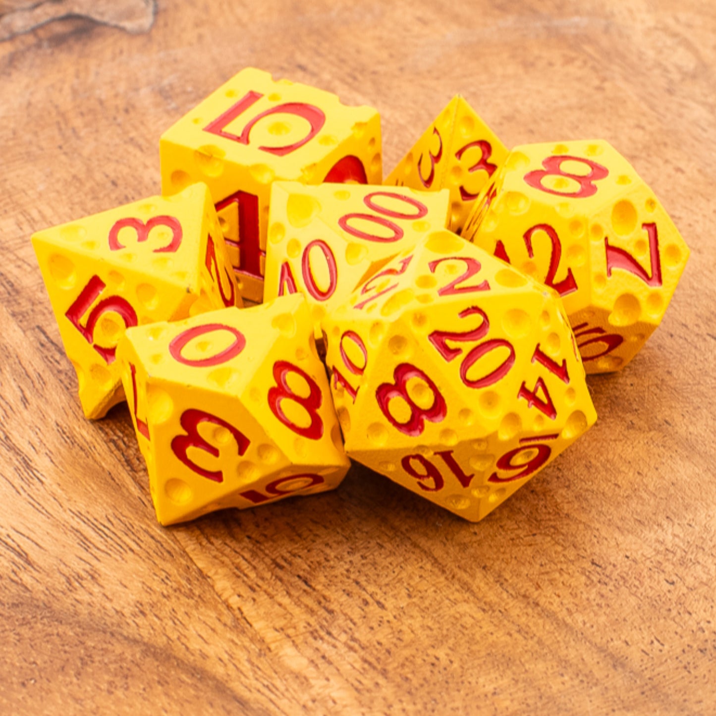 Tabletop Dominion Cheddar Champion heavy metal dice shown loose on a wooden surface, designed with a cheese‑like texture in yellow with red numbering.