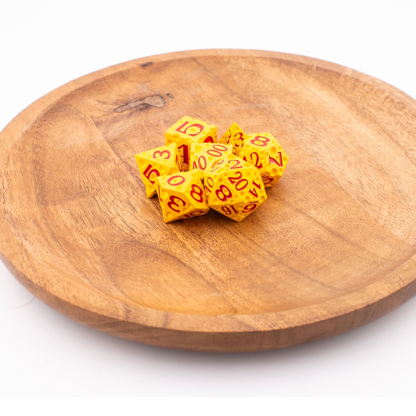 Tabletop Dominion Cheddar Champion heavy metal d20 dice arranged on a wooden plate, styled with a cheese‑like yellow texture and red numbering.