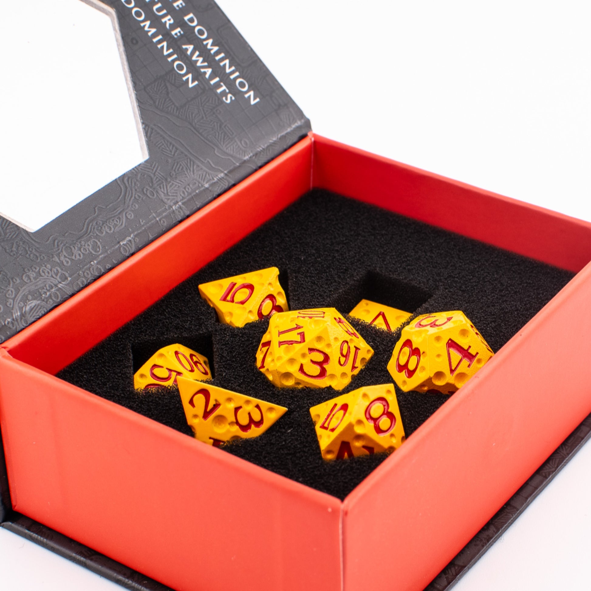 Tabletop Dominion Cheddar Champion heavy metal dice set displayed in an open box with yellow dice and red numbering in foam.