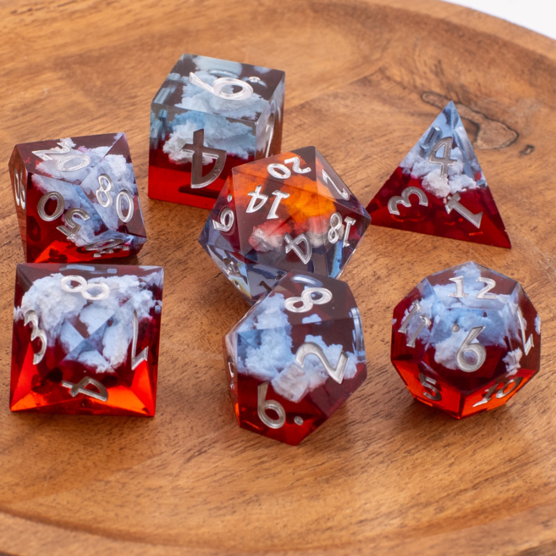 Ember Cloud sharp‑edge resin dice arranged neatly on a wooden background, showing all seven dice with swirling cloud inclusions and white numbering.